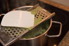 Der Spätzleteig wird durch ein Spätzlesieb in kochendes Wasser gedrückt
