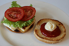 Salat und Tomaten auf den Käse geben und Ketchup und Mayonaise auf die Oberseite des Burger Bun